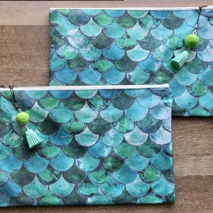 May include: Two zippered pouches with a mermaid scale pattern in shades of green and blue. Each pouch has a green tassel charm.
