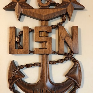 May include: A wooden US Navy anchor with two stars and the word "EBONY" engraved on the bottom. The anchor is brown and has a chain wrapped around it.