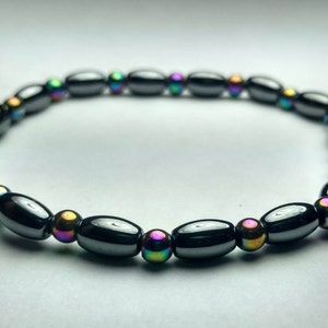 May include: A black bracelet with oval-shaped beads and iridescent round beads. The bracelet is made of hematite.