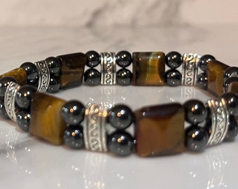 May include: A brown and gold tiger's eye stone bracelet with black hematite beads and silver spacers. The bracelet has a decorative design on the spacers.