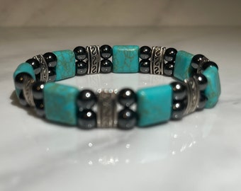 May include: A turquoise and black beaded bracelet with silver accents. The bracelet is made with square turquoise stones and round black beads.