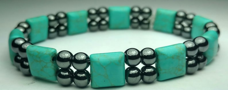 May include: A turquoise and black beaded bracelet with square turquoise beads and round black beads.