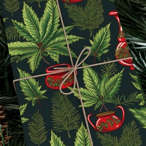 Op de afbeelding: Donkerblauw cadeaupapier met een herhalend patroon van groene bladeren en rode theepotten met bloemmotieven.