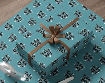 Może przedstawiać: Niebieski papier do pakowania z powtarzającym się wzorem białych gwiazdek i napisem "Baby Boy" w kolorze czarnym. Wstążka w kolorze brązowym jest zawiązana wokół pudełka prezentowego owiniętego tym samym papierem.