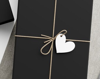 May include: Three black gift boxes wrapped with twine and white paper tags. The boxes are on a light brown fabric surface. One tag is a star shape, and the other is a heart shape.