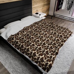 May include: A brown and beige leopard print throw blanket on a bed with a black headboard.