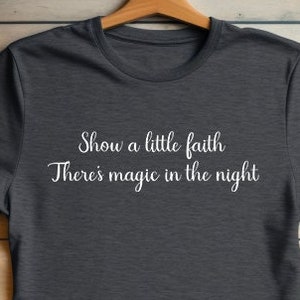 May include: A dark grey t-shirt with the text "Show a little faith There's magic in the night" printed in white on the front.