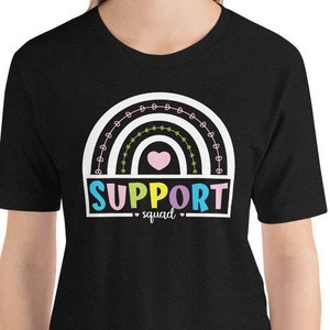 Puede incluir: Camiseta negra con un diseño de arcoíris blanco y el texto "SUPPORT squad" en letras de colores.