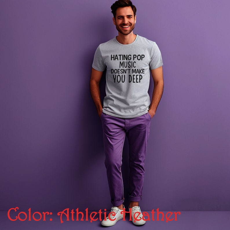 Puede incluir: Una camiseta gris con el texto "Hating Pop Music Doesn't Make You Deep" impreso en la parte delantera. La camiseta est&aacute; siendo modelada por una persona sobre un fondo morado.
