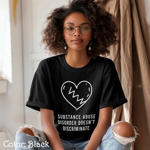 May include: A black t-shirt with a white broken heart graphic and the text "Substance Abuse Disorder Doesn't Discriminate".