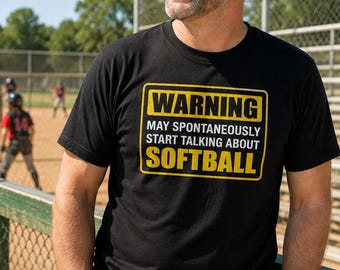 May include: A black short-sleeved t-shirt featuring a yellow rectangular border with the text "WARNING MAY SPONTANEOUSLY START TALKING ABOUT SOFTBALL" printed in white and yellow capital letters on the front of the garment.