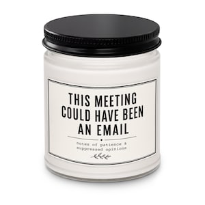 Peut inclure: Une bougie en pot de verre transparent avec un couvercle noir à vis, remplie de cire blanche. L'étiquette porte le texte noir : THIS MEETING COULD HAVE BEEN AN EMAIL, suivi du texte plus petit : notes of patience & suppressed opinions avec une icône de feuille.