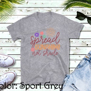 May include: A heather grey t-shirt with the text "Spread Sunshine not shade" in orange and brown lettering. The text is surrounded by small flowers and a sun graphic.