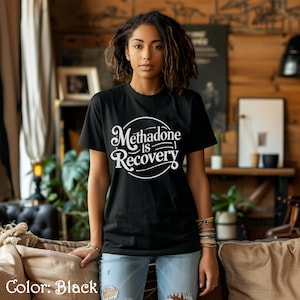 May include: Black crew neck t-shirt with the white text "Methadone is Recovery" in a circular design. The shirt is made of a soft material and is suitable for everyday wear. The shirt is a solid black color.