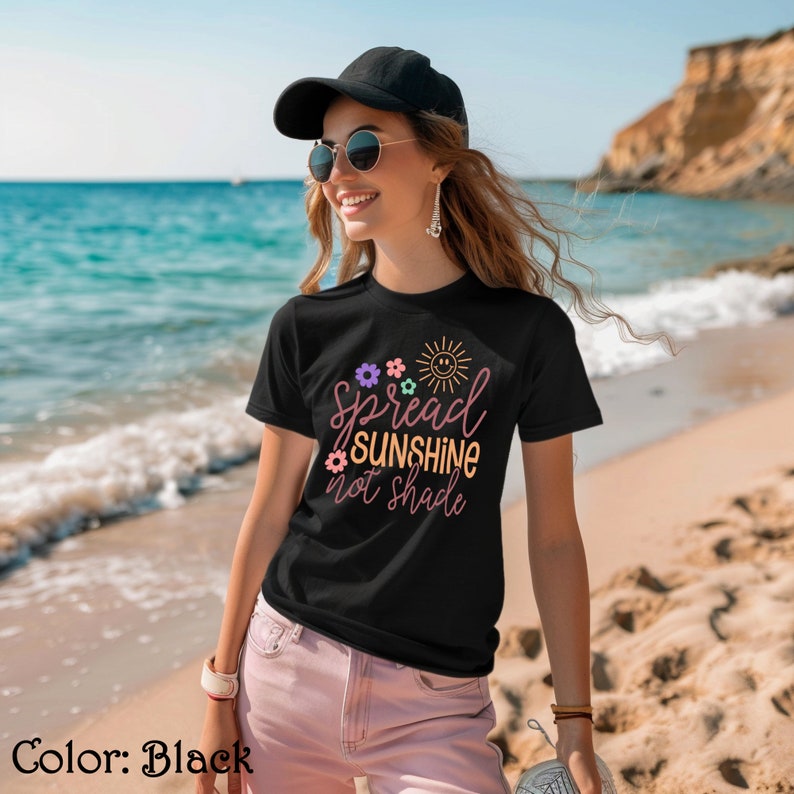 May include: A black t-shirt with a graphic that says "Spread Sunshine Not Shade" with a sun and flowers in pink, yellow, green, and purple.