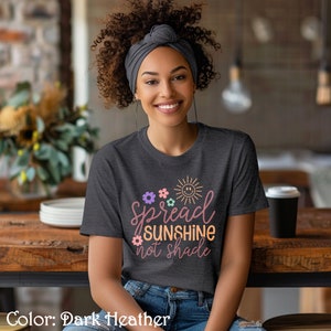 May include: A dark heather grey t-shirt with a graphic design that says "Spread Sunshine Not Shade" with a sun and flowers in pastel colors.