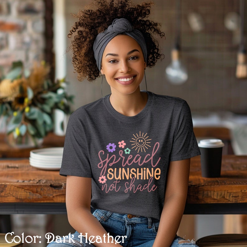 May include: A dark heather grey t-shirt with a graphic design that says "Spread Sunshine Not Shade" with a sun and flowers in pastel colors.