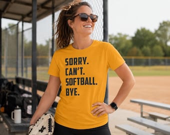 May include: A mustard yellow short-sleeved t-shirt featuring the black text SORRY. CAN'T. SOFTBALL. BYE. printed in a bold, sans-serif font on the front. The shirt has a crew neckline and a standard fit, providing a casual look for sports activities.
