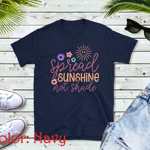 May include: Navy blue t-shirt with a graphic design featuring a sun with a smiley face, flowers, and the text "Spread Sunshine not Shade".