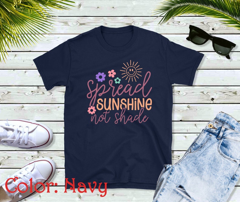 May include: Navy blue t-shirt with a graphic design featuring a sun with a smiley face, flowers, and the text "Spread Sunshine not Shade".