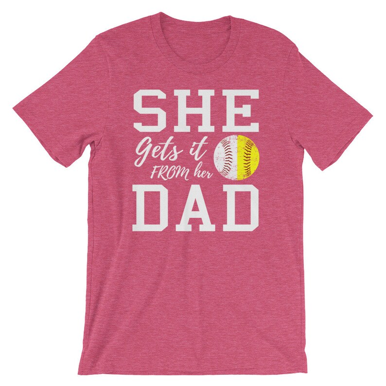 May include: Pink t-shirt with white text that reads "SHE gets it FROM her DAD" and a softball graphic.