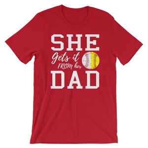 May include: Red t-shirt with white text that reads "SHE Gets it FROM her DAD" and a softball graphic.