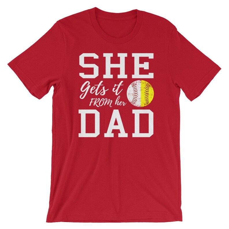 May include: Red t-shirt with white text that reads "SHE Gets it FROM her DAD" and a softball graphic.