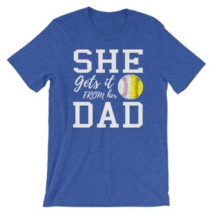 May include: Blue t-shirt with white text that reads "SHE gets it FROM her DAD" and a yellow softball graphic.