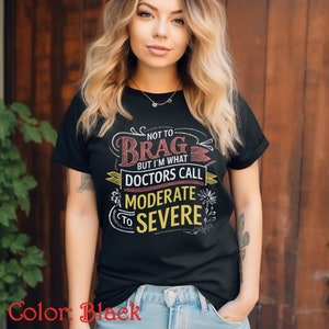 Puede incluir: Camiseta negra con un diseño gráfico blanco y amarillo que dice "Not to Brag but I'm what Doctors Call Moderate to Severe".