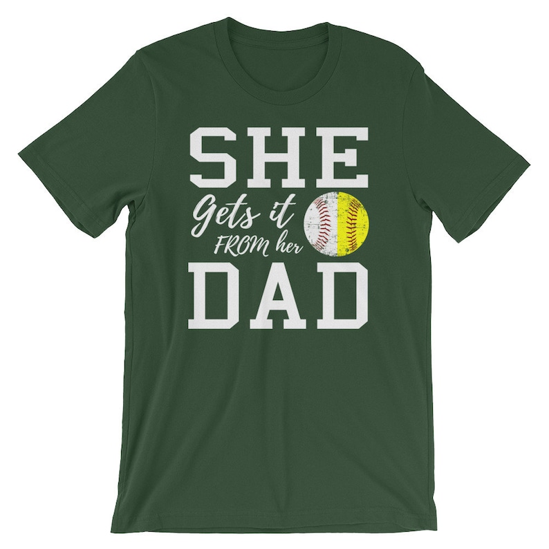May include: Green short-sleeved t-shirt with white text that reads "SHE gets it FROM her DAD" and a yellow softball graphic.