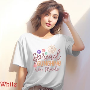 May include: White t-shirt with a graphic design that says "Spread Sunshine not Shade" with a sun and flowers in colorful hues.