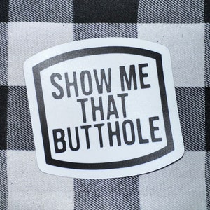 May include: White sticker with a black border and rounded corners. The sticker has the text "SHOW ME THAT BUTTHOLE" in black.