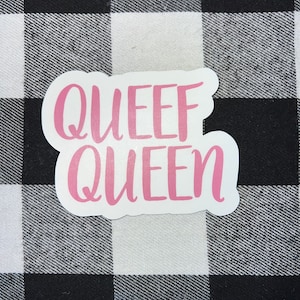 May include: Pink vinyl sticker with the text "Queef Queen" on a black and white checkered background.