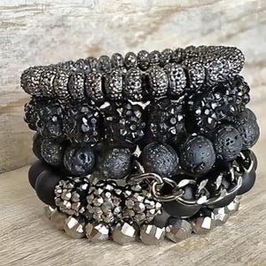 May include: A collection of black and silver beaded bracelets. The bracelets showcase diverse textures, such as smooth beads, textured beads, and chain links. The colour scheme is mainly black and silver, with a combination of matte and glossy finishes.