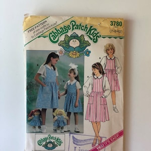 May include: Vintage Butterick sewing pattern for Cabbage Patch Kids outfits. The pattern shows illustrations of girls in dresses and aprons, with matching dolls. Includes the text "FREE PATTERN" and "YES! IT'S EASY!"