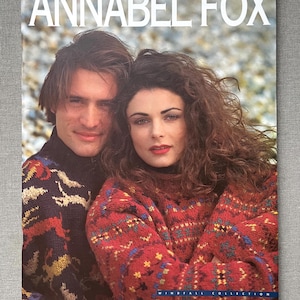 May include: A magazine cover with a man and a woman in patterned knitwear. The woman wears a red sweater with a geometric design, the man a dark blue one. The magazine title is "ANNABEL FOX". The words "WINDFALL COLLECTION" are also visible.
