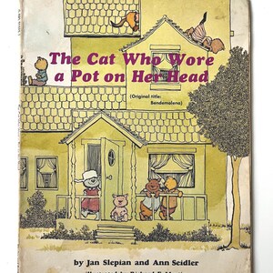 May include: A vintage children's book cover featuring a yellow house and a cat wearing a pot on its head. The book title is "The Cat Who Wore a Pot on Her Head", with the original title "Bendemolena" in brackets. The book is by Jan Slepian and Ann Seidler, illustrated by Richard E. Martin.