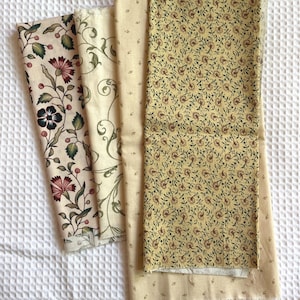 May include: Four fabric swatches with floral and botanical patterns. The fabrics feature cream, tan, and yellow backgrounds with designs in shades of red, green, and brown. The patterns include vines, flowers, and small sprigs.