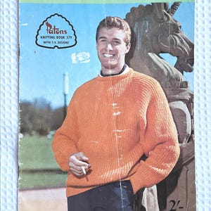 May include: A vintage Patons knitting book, No. 579, featuring a person wearing a bright orange ribbed jumper. The cover includes the text Totem, Highland Sports, Confetti Flecks, and Patons Knitting Book 579 with T.V. Designs, alongside a unicorn statue.