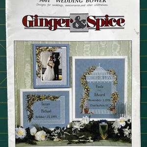 May include: A vintage wedding design book titled "Wedding Bower" by Ginger & Spice. The cover features framed cross-stitch designs with wedding themes, including names and dates. The designs are framed with floral arrangements.