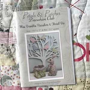 May include: A Petals & Patches pincushion and thread bin package. The design includes a tree with birds, a small fabric bin, and a bunny. The package size is 14 cm x 7.6 cm, and the bin is 6.35 cm square.