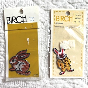 May include: Two iron-on embroidered rabbit patches. One is brown and white, the other wears a yellow suit. Both are on yellow backing cards, branded "BIRCH". The patches are ideal for fabric decoration.