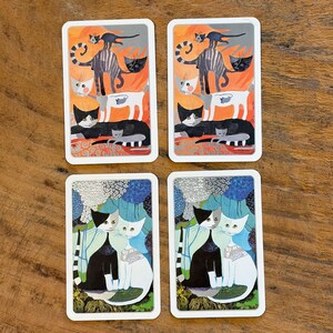 May include: Four rectangular cat-themed coasters. Two coasters feature a design with orange, black, and white cats. The other two coasters have a design with black and white cats against a blue and green background.