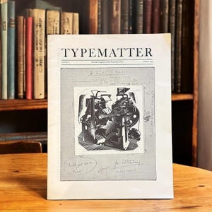 Könnte beinhalten: Eine Schwarzweißillustration einer Druckpresse auf grauem Hintergrund. Der Text "TYPEMATTER" befindet sich oben auf der Seite. Der Text "3 2 INCOS PRESS" und "3 1/2 ONE AS THE" ist auf dem Bild geschrieben. Der Text "ONE TURNED LEFT RIGHT" ist auf dem Bild geschrieben.