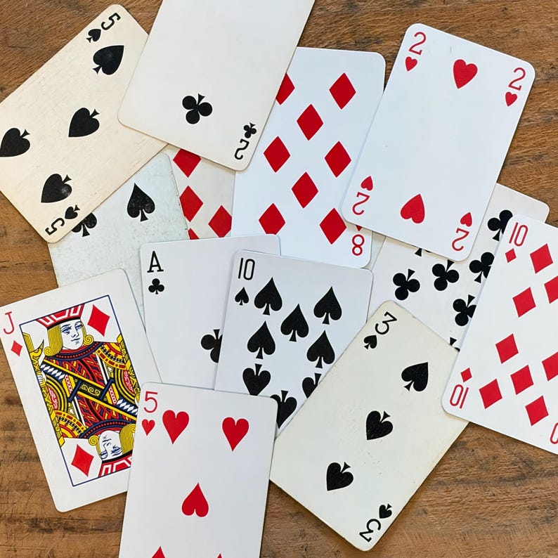 May include: A collection of scattered playing cards featuring various suits and ranks, including a Jack of diamonds, a five of spades, a two of hearts, a ten of spades, and a ten of diamonds, all displayed with their white faces and colorful pips.