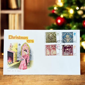 以下が含まれることがあります： 「Christmas 1976」の文字が黄色で書かれた白い封筒。封筒には、暖炉のそばでピンク色のローブを着た人物の初日発行イラストが描かれています。4枚の切手が右上に貼られています。