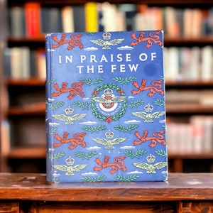 Könnte beinhalten: Ein blaues Hardcover-Buch mit dem Titel "In Praise of the Few" auf dem vorderen Umschlag. Der Umschlag zeigt ein sich wiederholendes Muster aus roten Löwen, grünen Blättern und geflügelten Emblemen.