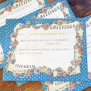 May include: A blue and white telegram with a floral border and stars. The text reads "Greetings Betty and John 21 St. Margarets Avenue N15- Heartiest Congratulations and Good Luck = Bert Ivy and Brian" and "Telegram".