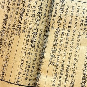 May include: A page of antique paper featuring vertical columns of traditional Chinese characters printed in black ink. The paper has a light tan, aged appearance with visible texture and vertical lines separating the columns of text throughout the page.