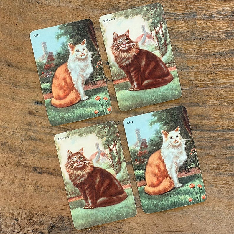 May include: Four vintage cat-themed playing cards. Two cards are labeled "Ken" and two are labeled "Tarzan". Each card features a different cat illustration set against a background of a garden and a building.